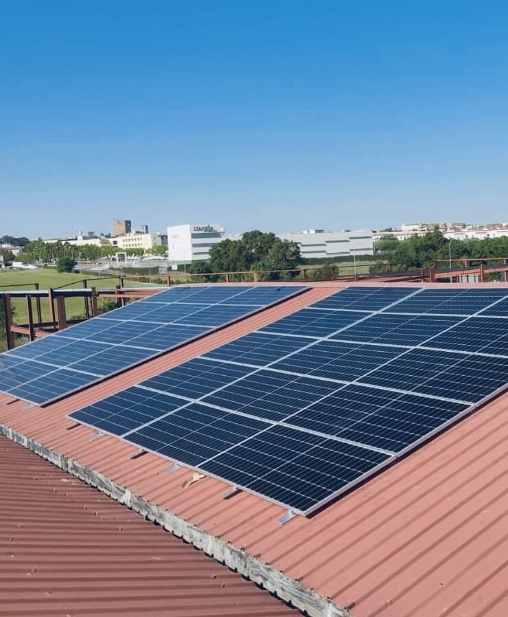 Paneles solares en azotea roja, edificios al fondo.