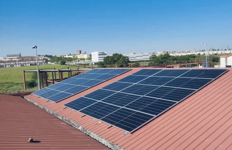 Paneles solares en azotea roja, edificios al fondo.