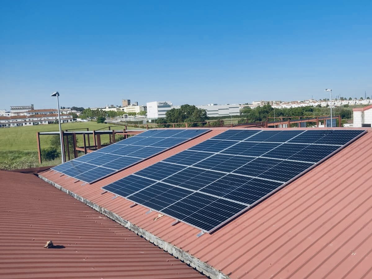 Paneles solares en azotea roja, edificios al fondo.